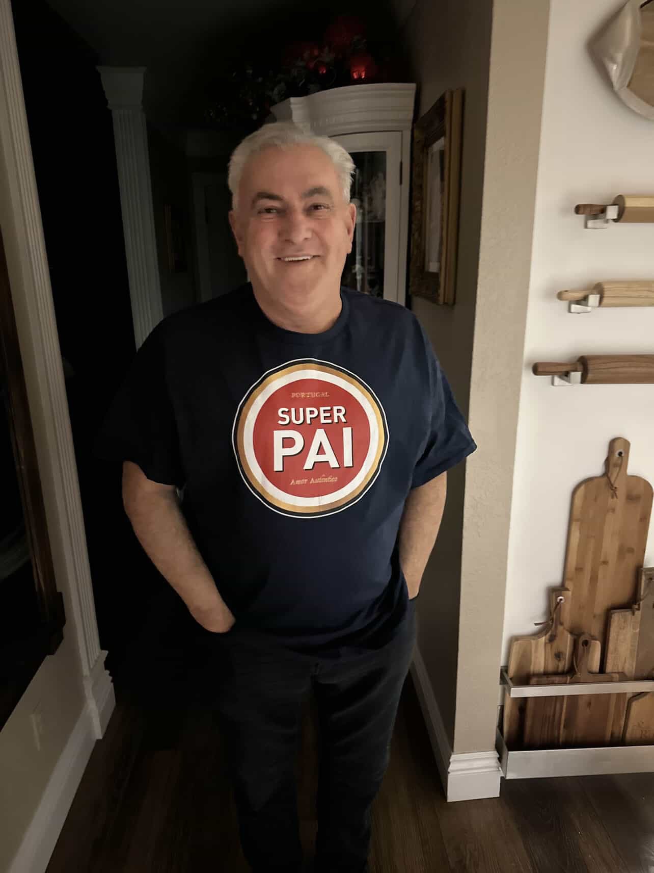 Man wearing a black t-shirt with a 'Super Pai, amor autêntico' graphic in a home setting