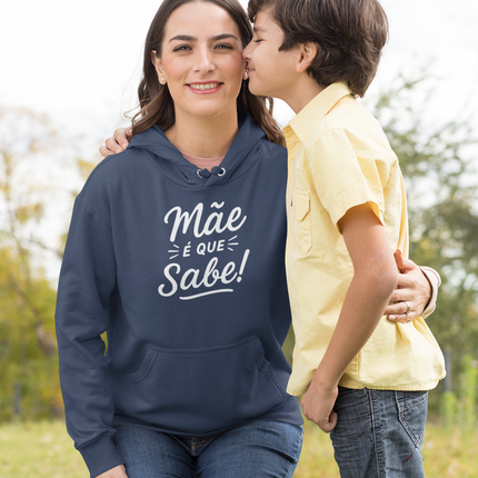 Woman wearing a navy hoodie with "Mãe é que sabe!" text and a child kissing her outdoors.