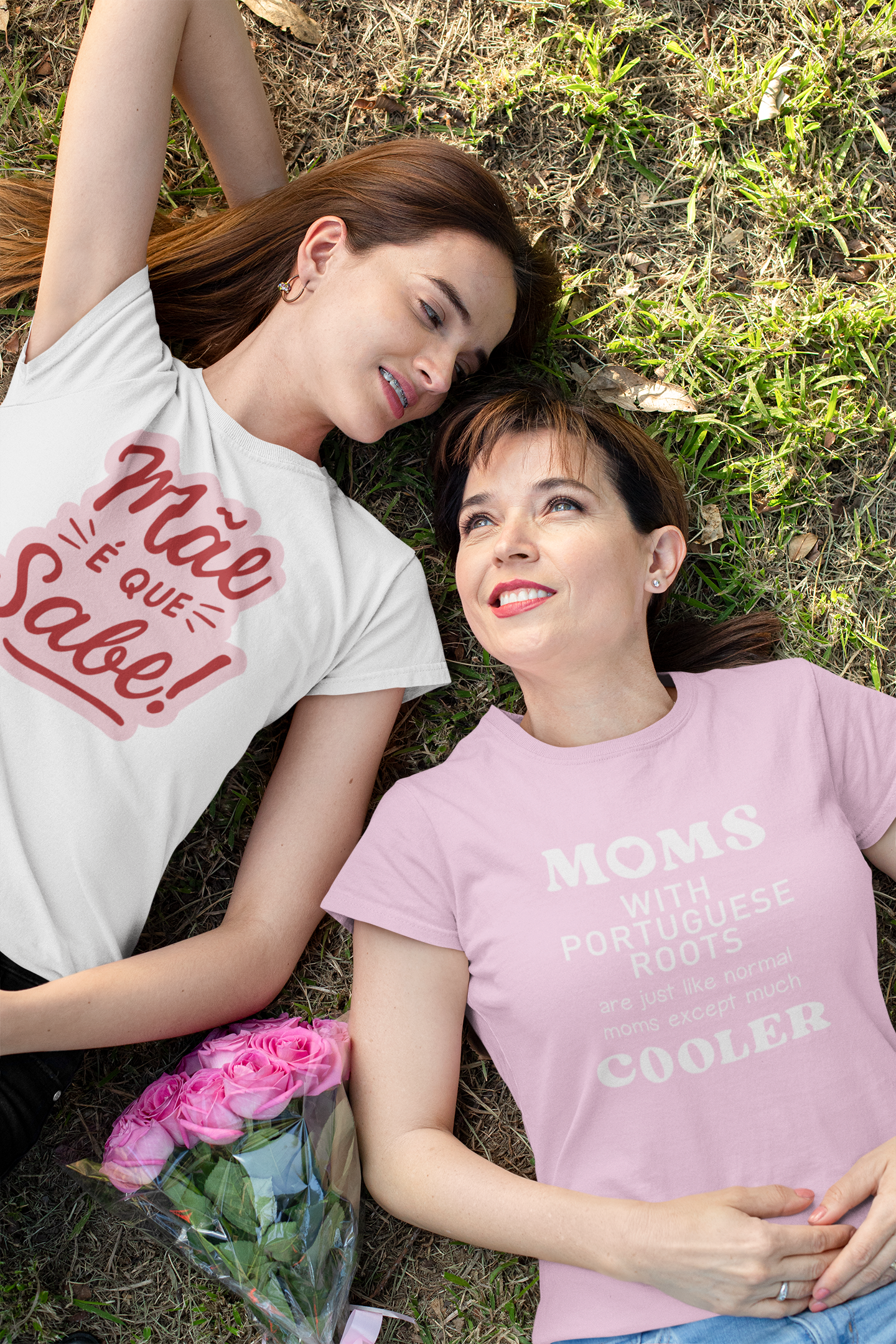 Two women lying on grass wearing t-shirts with text, one white and one pink.