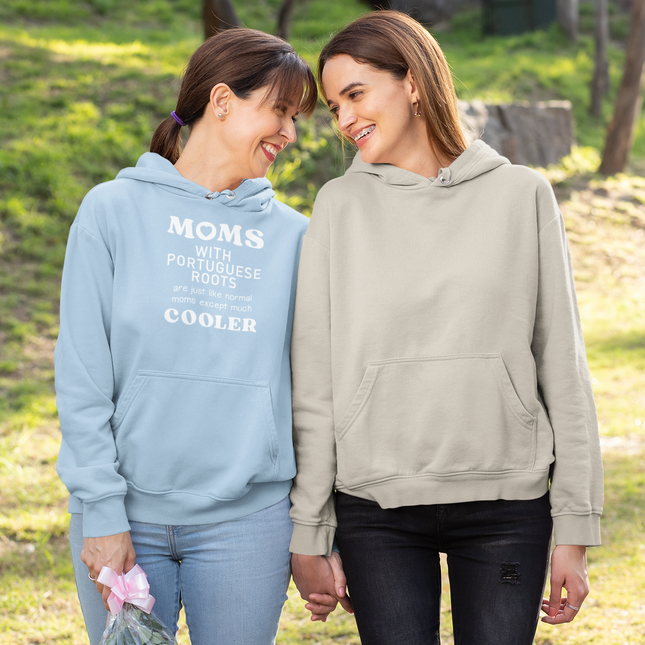 Two women standing outdoors, one wearing a blue hoodie with "Moms with portuguese roots are just like normal moms, except much cooler " text and the other in a beige hoodie.