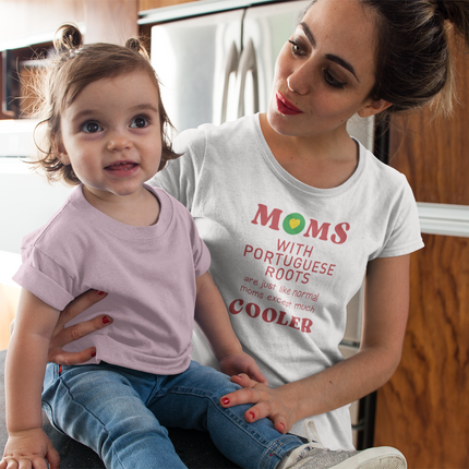 Woman wearing a t-shirt with "Moms with portuguese roots are just like normal moms except much cooler" text sitting on a couch with a child.