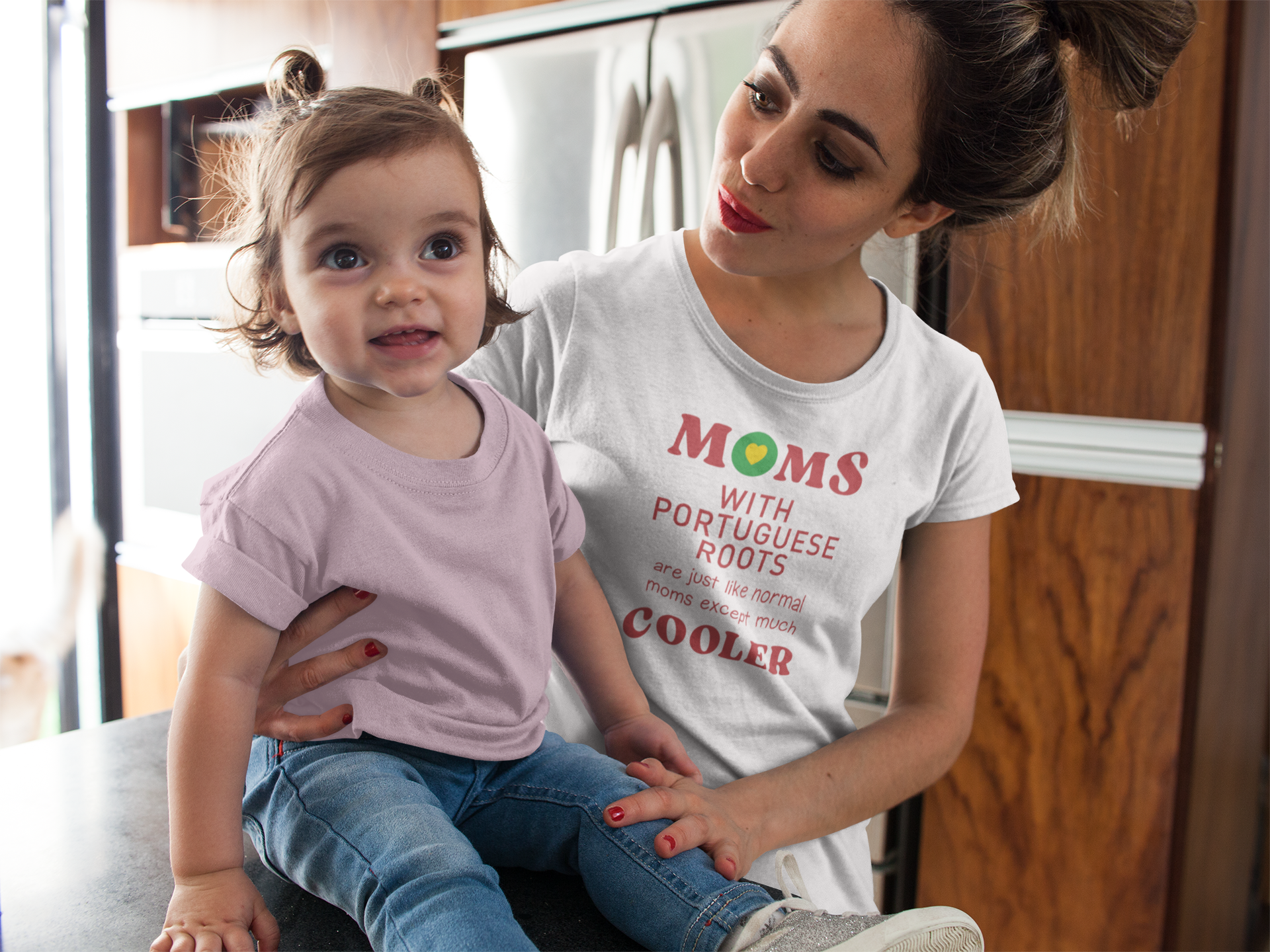 Woman wearing a t-shirt with "Moms with portuguese roots are just like normal moms except much cooler" text sitting on a couch with a child.