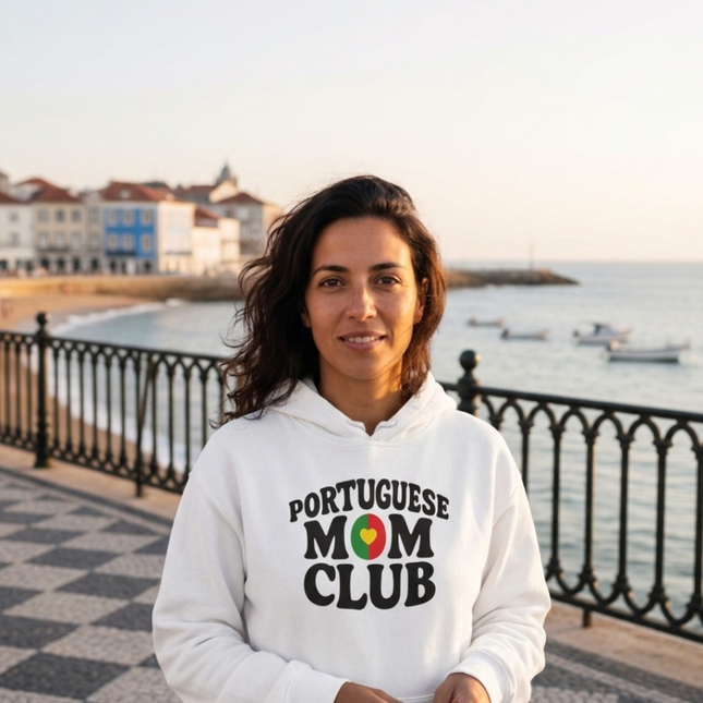 Woman wearing a 'Portuguese Mom Club' hoodie by a waterfront with buildings and boats in the background.