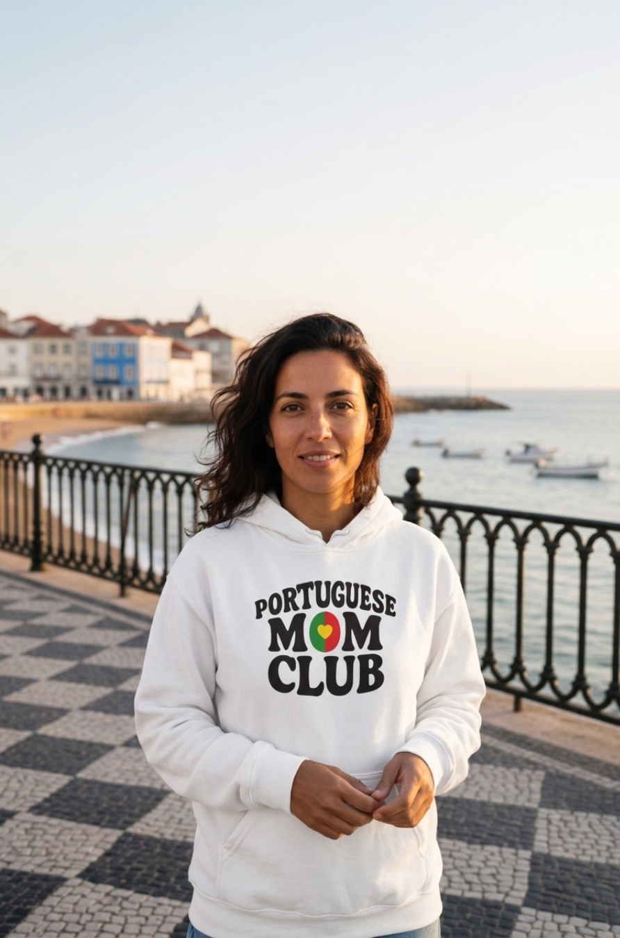 Woman wearing a 'Portuguese Mom Club' hoodie by a waterfront with buildings and boats in the background.