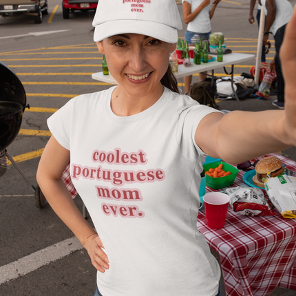 Woman wearing a white t-shirt with 'coolest portuguese mom ever' text, taking a selfie in a parking lot.