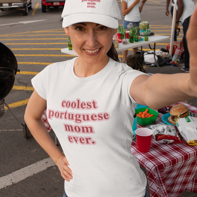 Woman wearing a white t-shirt with 'coolest portuguese mom ever' text, taking a selfie in a parking lot.