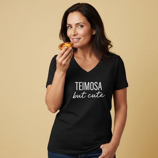 Woman wearing a black t-shirt with 'TEIMOSA but cute' text, holding a pastel de nata against a beige background